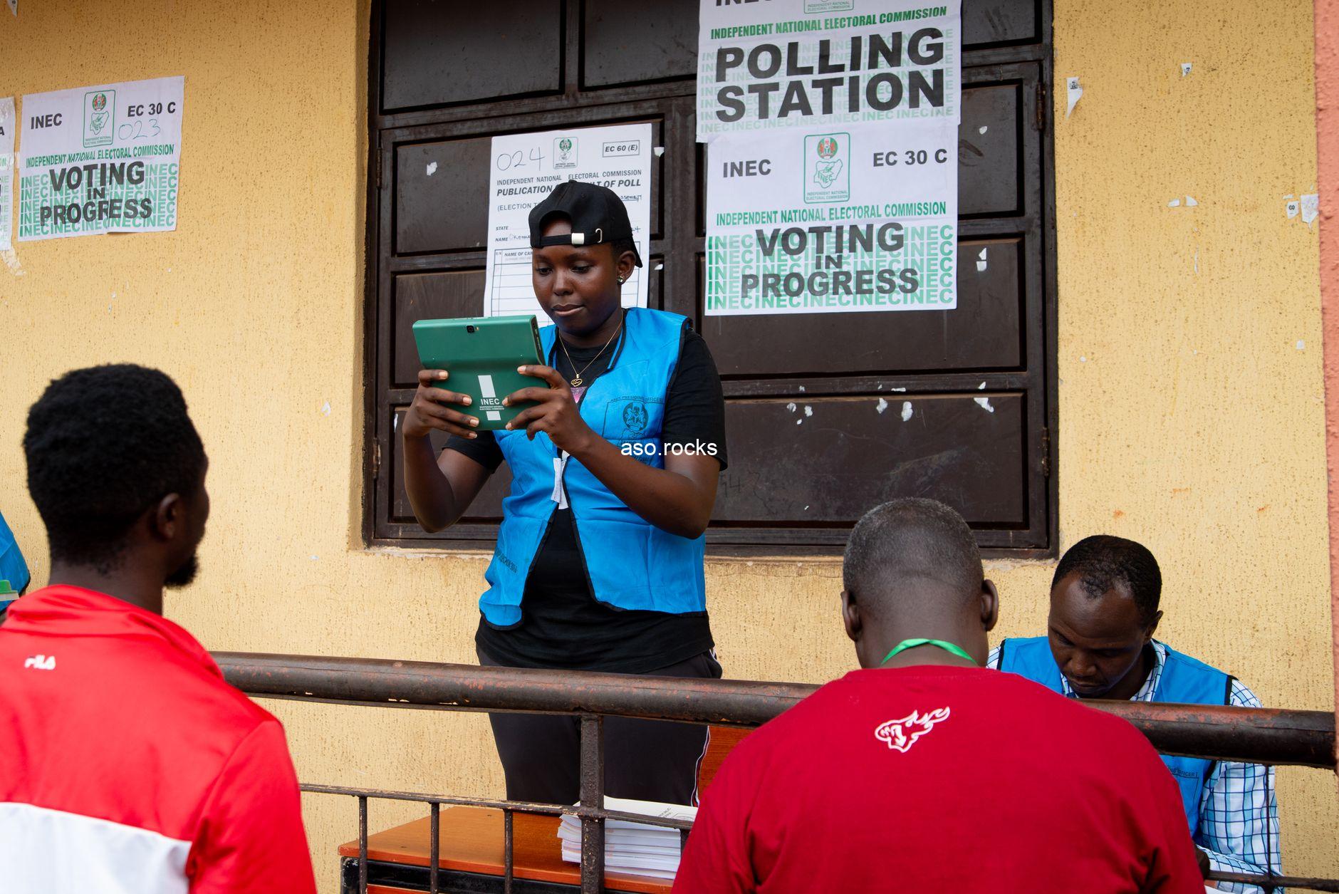 INEC election official at a Nigerian polling station on voting day, with Voting In Progress signage visible