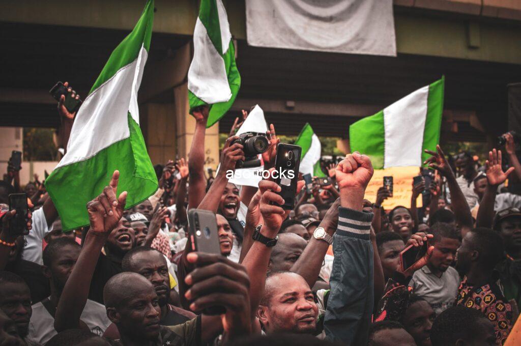 A large crowd of Nigerians waving green-and-white national flags at an outdoor political gathering